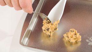 man's hands putting chocolate chip cookie dough on baking sheet